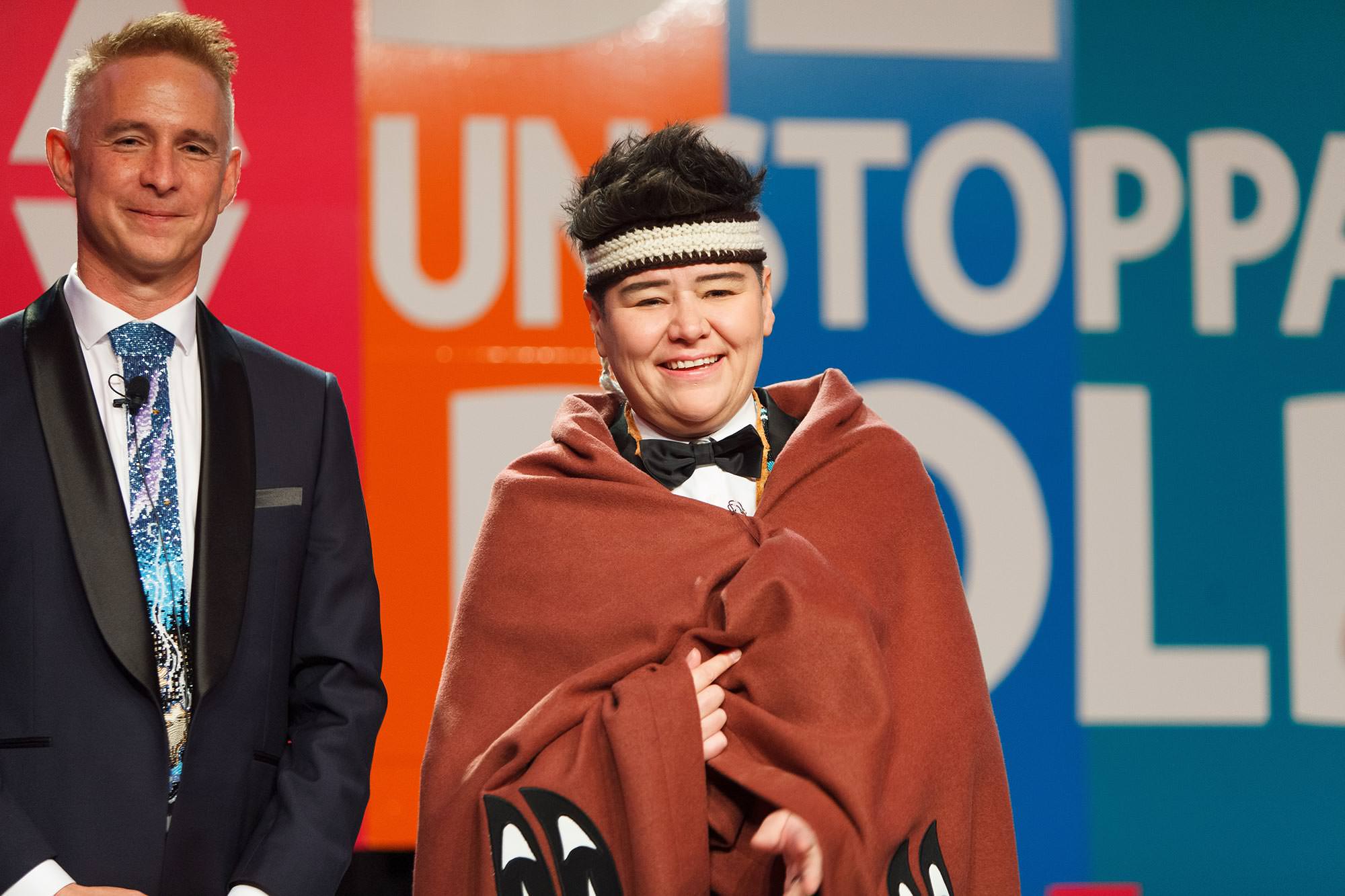 Bobby Racette and Paul Lacerte stand together in front of a vibrant backdrop with the word “UNSTOPPABLE” in multicolored letters, during DEYA 2023 at the Victoria Conference Centre.