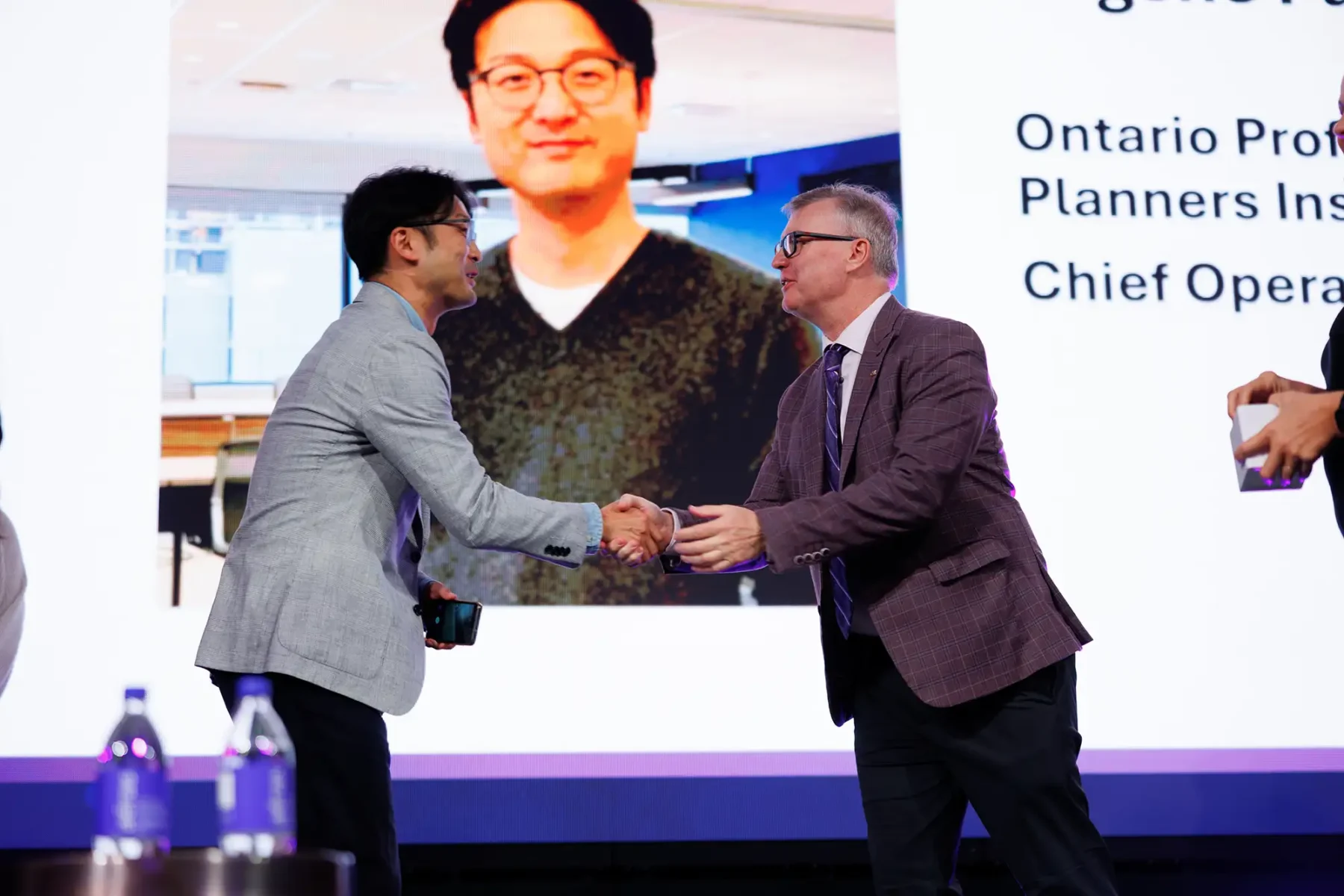 A sponsor shakes hands with a conference attendee on stage at the Victoria Conference Centre
