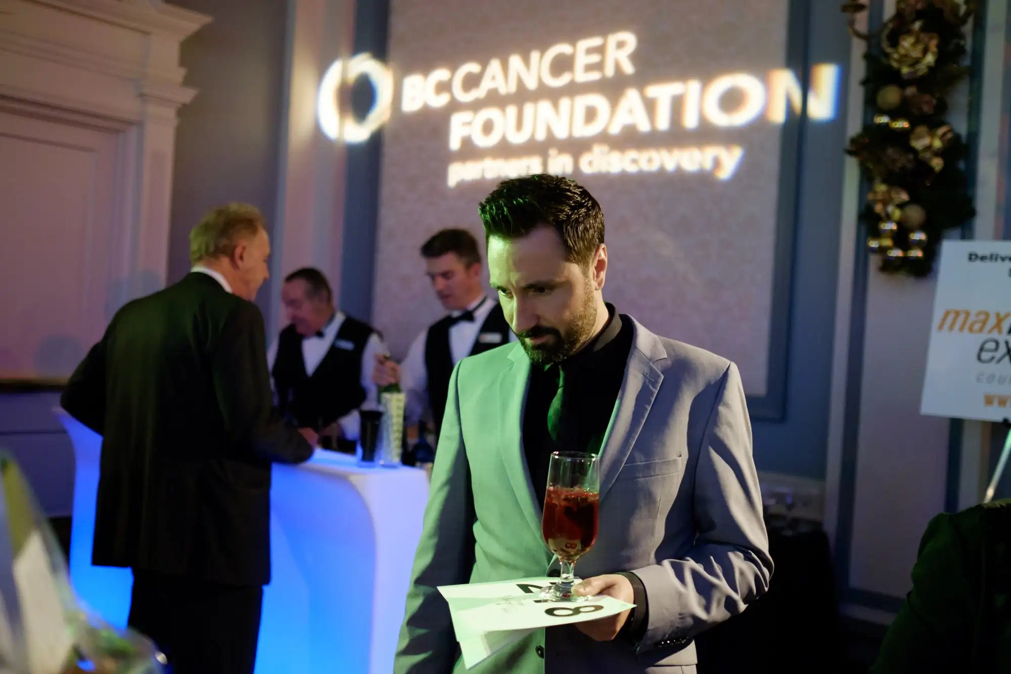 Man holding a cocktail glass while viewing auction items at the BC Cancer Foundation Jingle Mingle fundraising event in Victoria – event photography coverage
