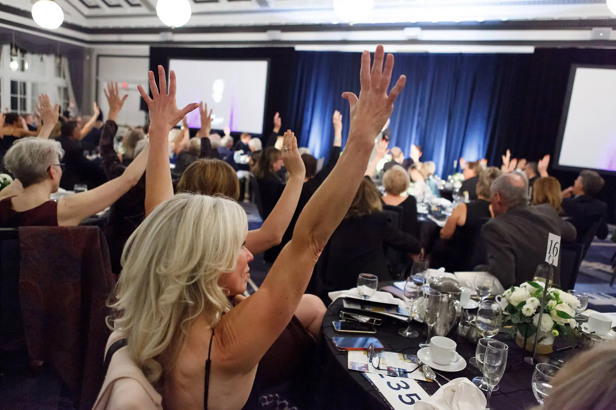 attendees at a non-profit fundraising dinner raise their hands in support of the cause at the fairmont empress in Victoria